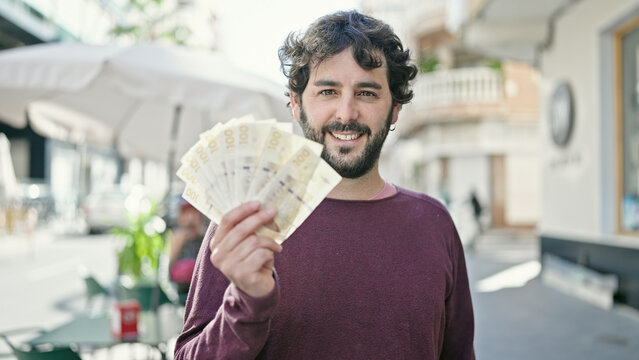 Young hispanic man smiling confident holding denmark krone banknotes at coffee shop terrace