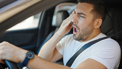 Young hispanic man tired driving car yawning at street