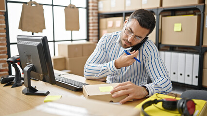 Young hispanic man ecommerce business worker talking on smartphone writing on package at office