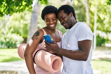 African american man and woman couple holding yoga mat using smartphone at park