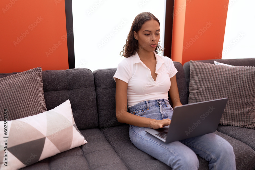 Poster young african american woman using laptop sitting on sofa at home