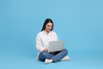 Smiling young woman working with laptop on light blue background. Space for text