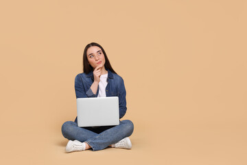 Naklejka premium Thoughtful young woman with laptop on beige background, space for text
