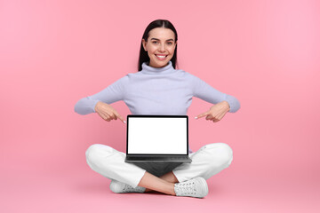 Happy woman pointing at laptop on pink background
