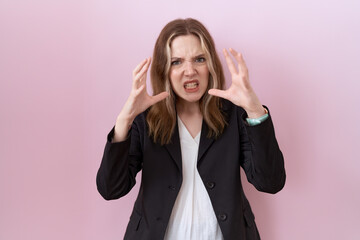 Young caucasian business woman wearing black jacket shouting frustrated with rage, hands trying to strangle, yelling mad