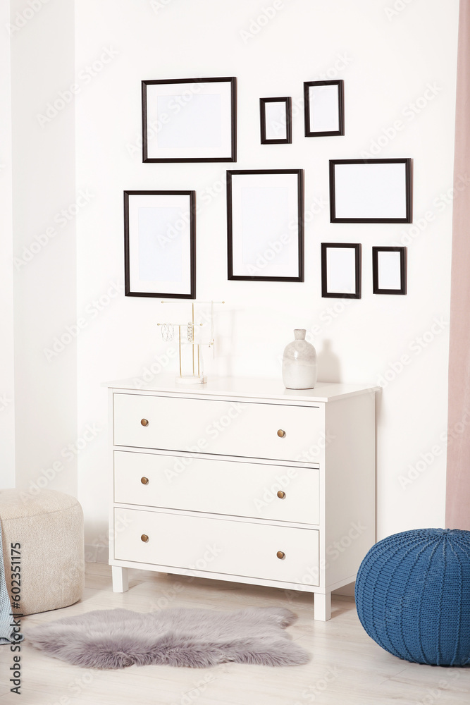 Poster Empty frames hanging on white wall, chest of drawers and ottomans indoors