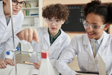 Portrait of boy doing science experiment in school classroom with group of children wearing lab coats