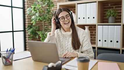 Young beautiful hispanic woman business worker using laptop and headphones working at office