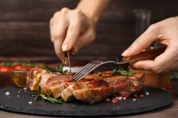 Woman eating delicious fried meat with rosemary and spices at table, closeup