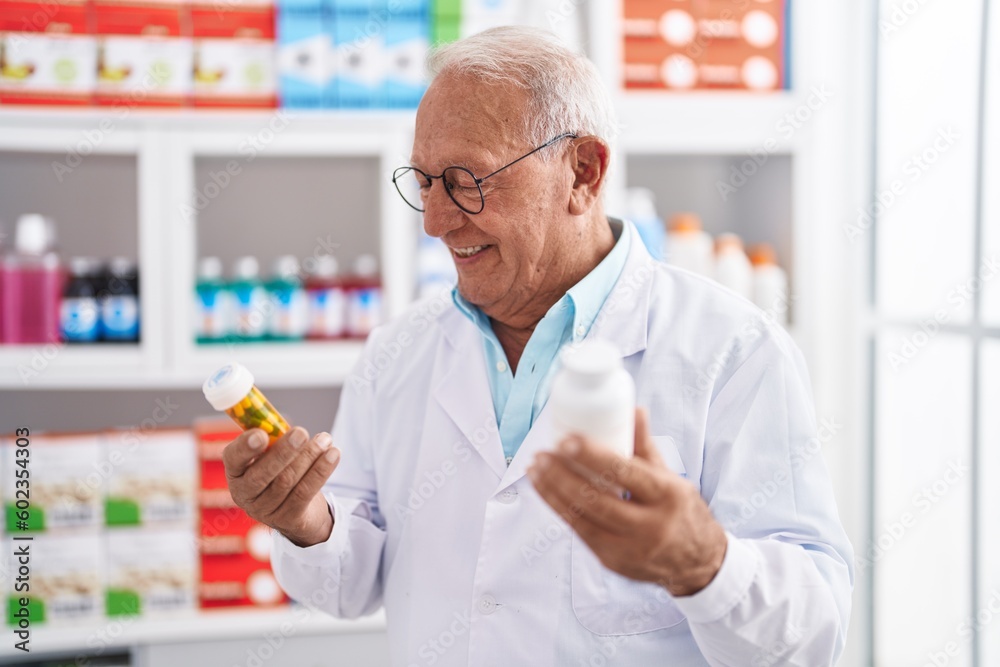 Wall mural senior grey-haired man pharmacist smiling confident holding pills bottles at pharmacy