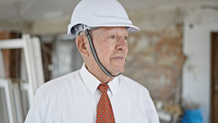 Senior grey-haired man architect standing with relaxed expression at construction site