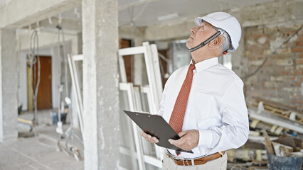 Senior grey-haired man architect holding clipboard looking around at construction site