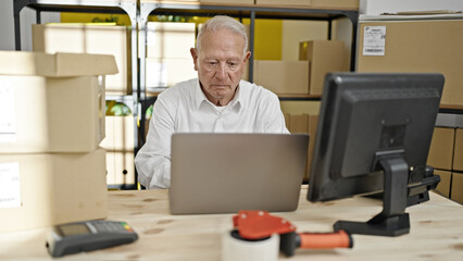 Senior grey-haired man ecommerce business worker using laptop working at office