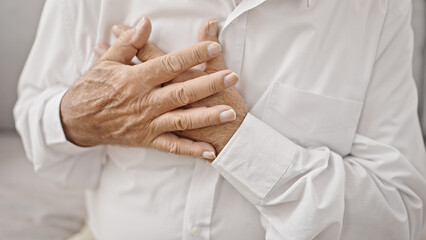 Senior grey-haired man sitting on sofa suffering heart attack at home