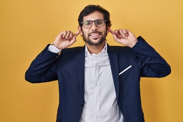 Handsome latin man standing over yellow background smiling pulling ears with fingers, funny gesture. audition problem