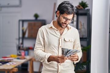 Young hispanic man artist smiling confident counting dollars at art studio