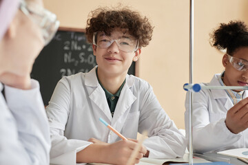 Portrait of smiling schoolboy with curly hair enjoying science class and looking at camera