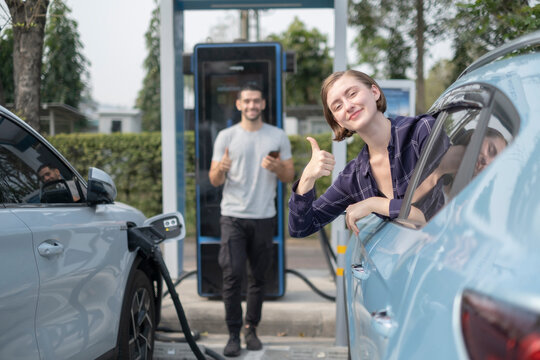 White woman show thumb up to camera with little smile at Electral car add fluel station, saving money and world with good qualiti of green energy.