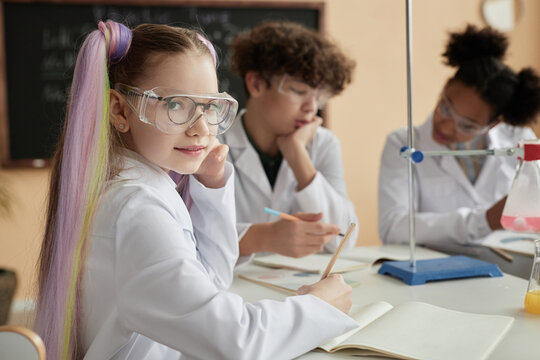 Portrait of cute schoolgirl with pigtails enjoying science class and looking at camera, copy space - Powered by Adobe