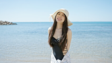 Young chinese woman tourist smiling confident wearing swimsuit and summer hat at seaside - obrazy, fototapety, plakaty