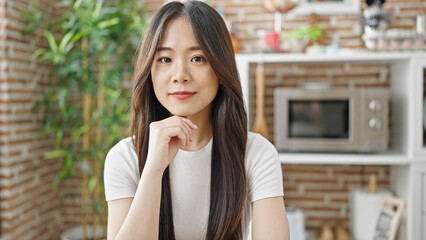 Young chinese woman sitting on table with relaxed expression at dinning room