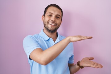 Hispanic man standing over pink background gesturing with hands showing big and large size sign, measure symbol. smiling looking at the camera. measuring concept.