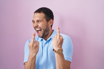 Hispanic man standing over pink background showing middle finger doing fuck you bad expression,...