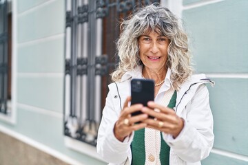 Middle age woman smiling confident using smartphone at street