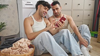 Two men couple using smartphone waiting for washing machine at laundry room