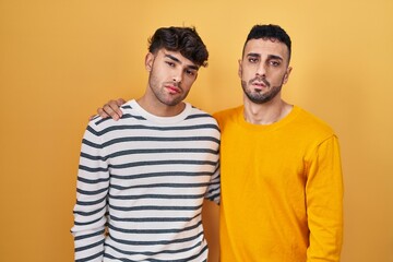 Young hispanic gay couple standing over yellow background looking sleepy and tired, exhausted for fatigue and hangover, lazy eyes in the morning.