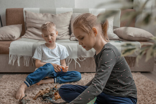 The younger brother and sister play with plastic animals sitting on the floor.Love and friendship within the family, joint leisure.Development of communication skills through the game