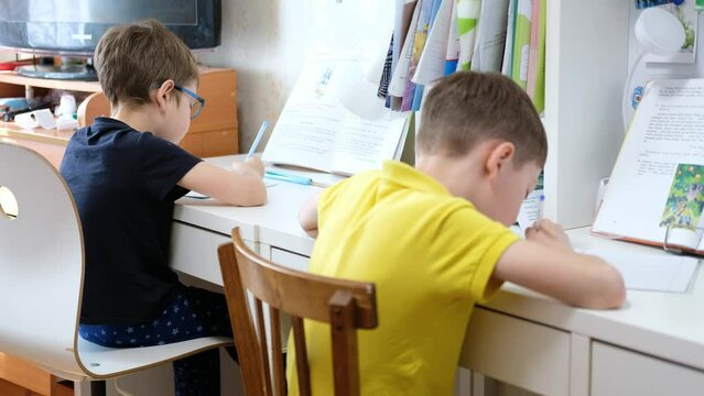 2 boys sit and write in notebooks at the table, at home. Two brothers do their homework. Homeschooling two boys