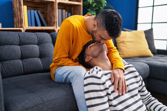 Two man couple hugging each other and kissing sitting on sofa at home