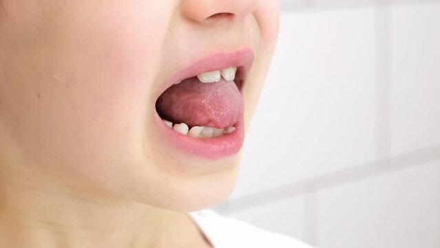 Child shows his loose milk tooth presses and pushes it with his tongue. Open mouth close-up. Caucasian 6 year old kid in a white T-shirt on a bathroom background. lower incisor. Copy space. Body part.
