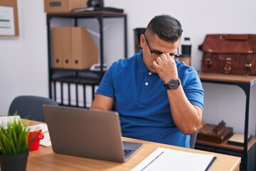 Young hispanic man working at the office with laptop tired rubbing nose and eyes feeling fatigue and headache. stress and frustration concept.