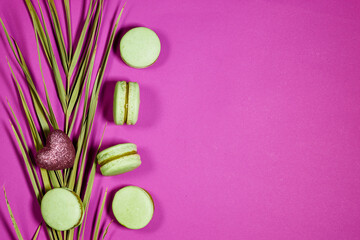 Obraz na płótnie Canvas French pistachio macarons and palm leaf and heart glitter on purple background with copy space 