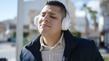 Young hispanic man listening to music and dancing at street