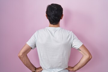 Obraz premium Young hispanic man standing over pink background standing backwards looking away with arms on body