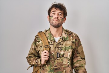 Hispanic young man wearing camouflage army uniform relaxed with serious expression on face. simple and natural looking at the camera.