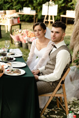 satisfied bride and groom are sitting at the wedding table outside. banquet after the wedding ceremony. wedding couple celebrating. wedding catering