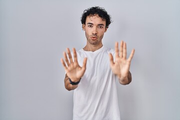 Naklejka premium Hispanic man standing over isolated background moving away hands palms showing refusal and denial with afraid and disgusting expression. stop and forbidden.