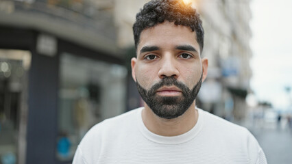 Young hispanic man standing with serious expression at street