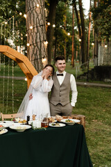 young and beautiful bride and groom are sitting at the wedding table on the background of the arch....