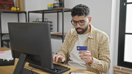 Young hispanic man business worker using computer and credit card at office