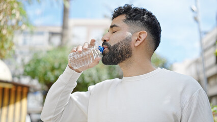 Young hispanic man drinking water at park