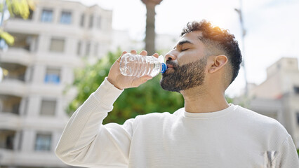 Young hispanic man drinking water at park