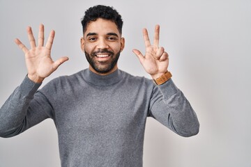 Fototapeta premium Hispanic man with beard standing over white background showing and pointing up with fingers number eight while smiling confident and happy.