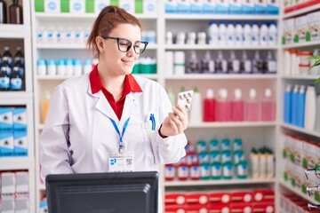 Young beautiful plus size woman pharmacist using computer holding pills tablet at pharmacy