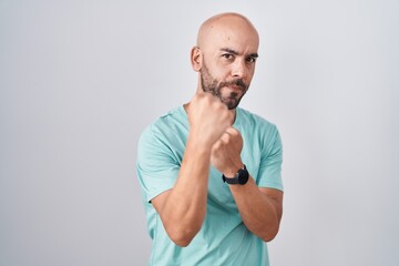 Middle age bald man standing over white background ready to fight with fist defense gesture, angry...