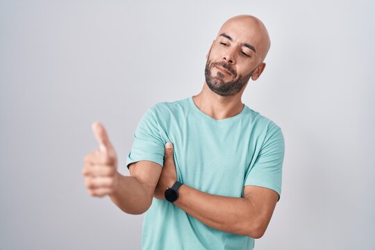 Middle age bald man standing over white background looking proud, smiling doing thumbs up gesture to the side